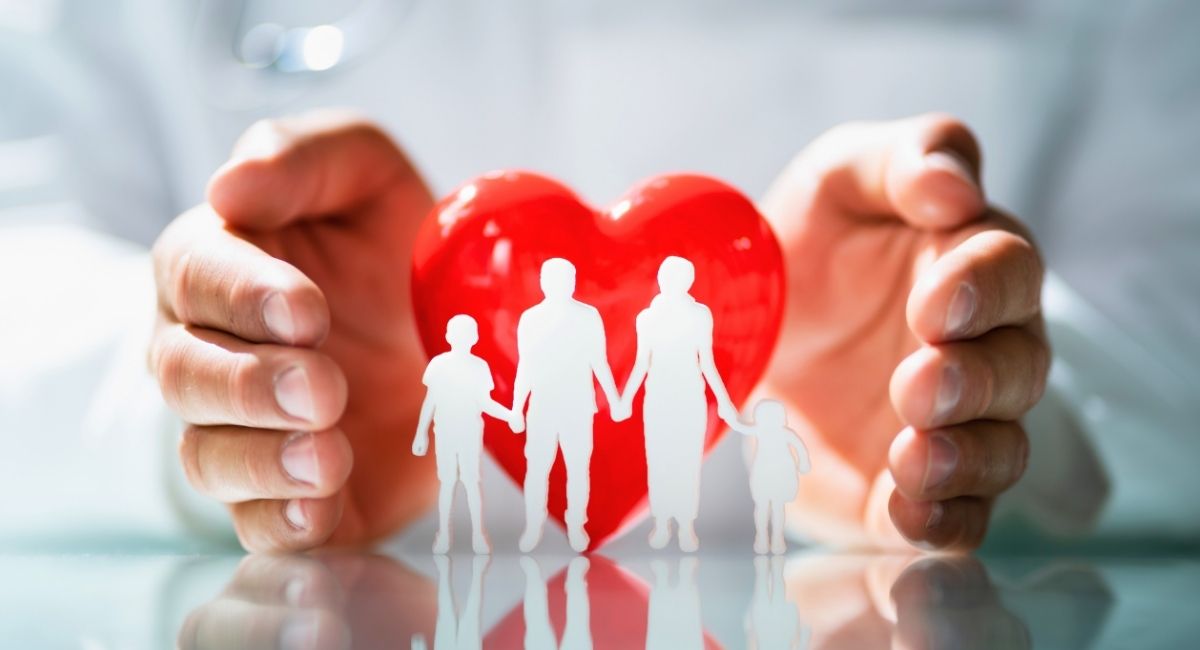 Mãos segurando um coração vermelho com silhuetas de uma família, simbolizando cuidado, proteção e bem estar familiar.